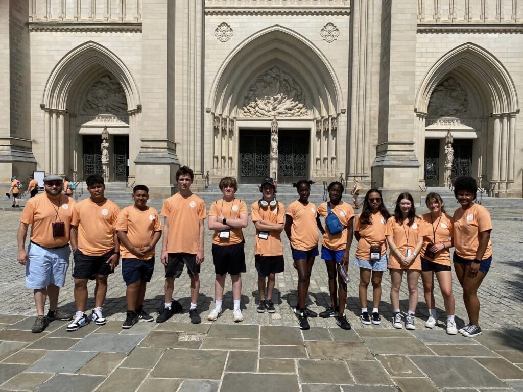 CEC and DioBeth youth in orange t-shirts stand in front of the Cathedral