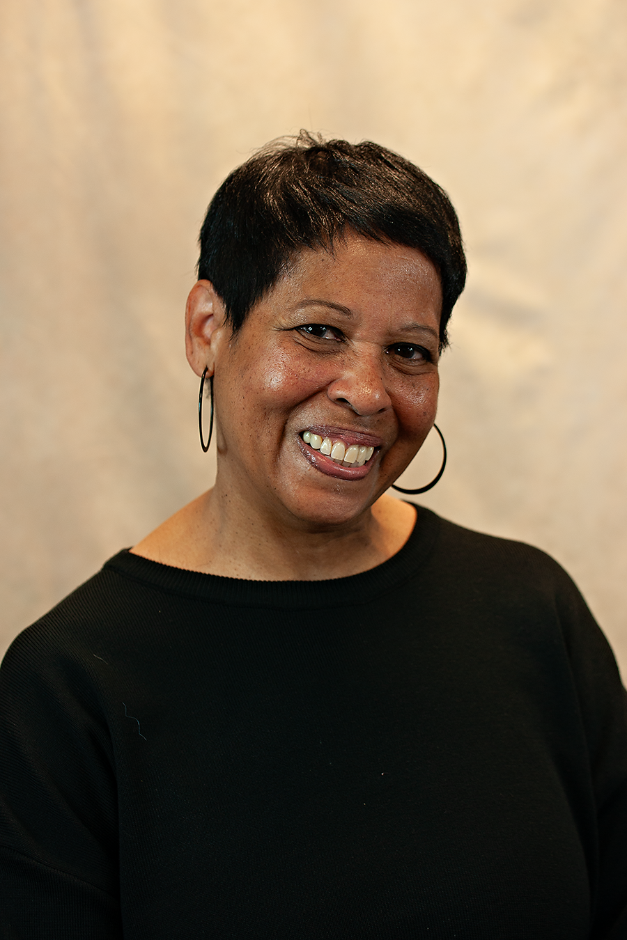 Smiling, professional black woman wearing a black top and hoop earrings.