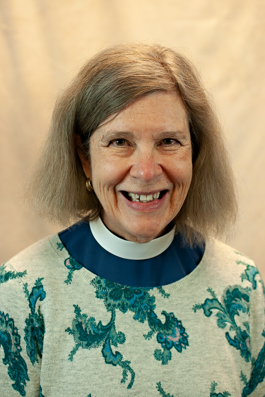 Rev. Dr. Sidnie White-Crawford, wearing a priest's collar and a floral sweater. She is smiling.